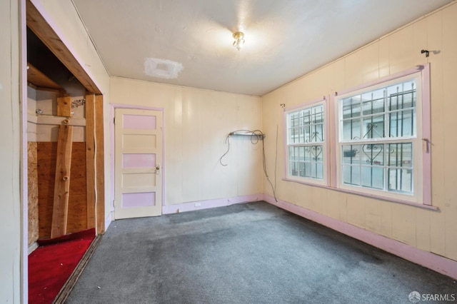 spare room featuring dark colored carpet and wooden walls