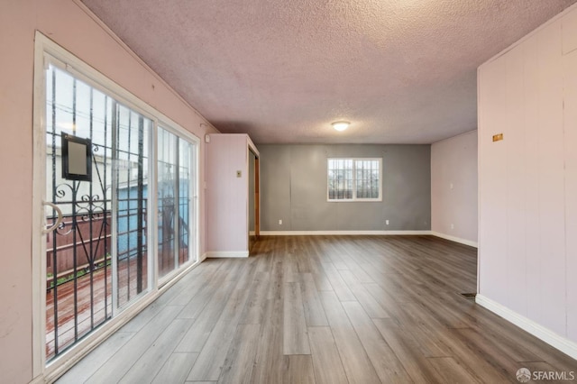 unfurnished room with a textured ceiling, wood finished floors, and baseboards