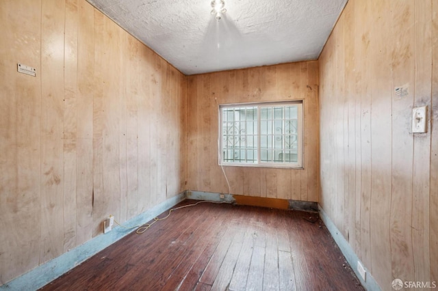 spare room with a textured ceiling, wooden walls, dark wood finished floors, and baseboards