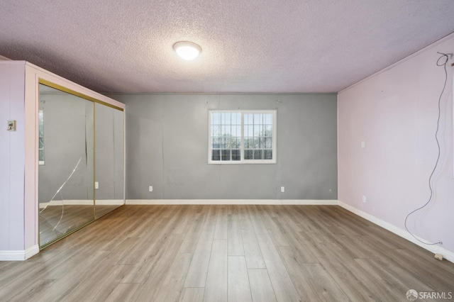 empty room with a textured ceiling, baseboards, and light wood-style floors