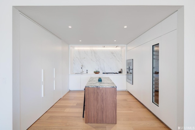 kitchen featuring decorative backsplash, a kitchen island, light wood-type flooring, and white cabinetry