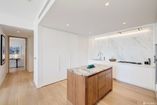 kitchen featuring sink, a kitchen island, light hardwood / wood-style flooring, backsplash, and white cabinets