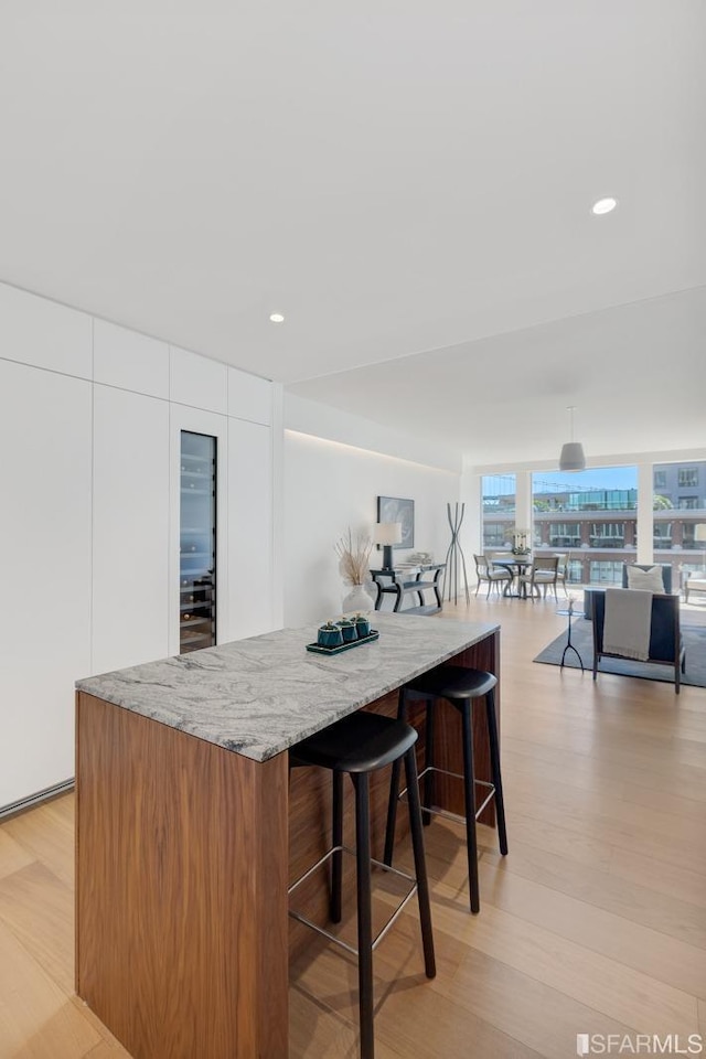 kitchen featuring white cabinetry, light stone countertops, light hardwood / wood-style flooring, pendant lighting, and a kitchen island