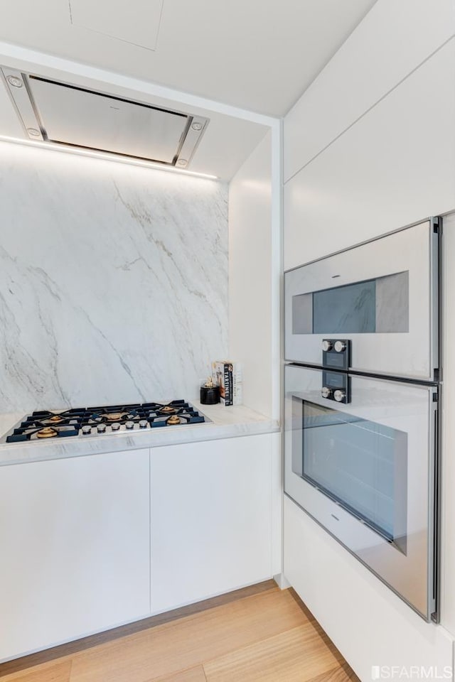 kitchen featuring white cabinetry, stainless steel double oven, and light hardwood / wood-style floors