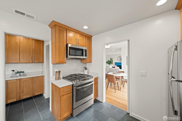 kitchen featuring decorative backsplash, visible vents, stainless steel appliances, light countertops, and dark tile patterned floors