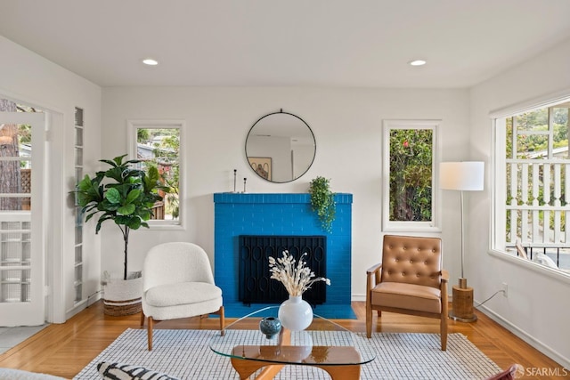 living area with recessed lighting, wood finished floors, a wealth of natural light, and a fireplace with flush hearth