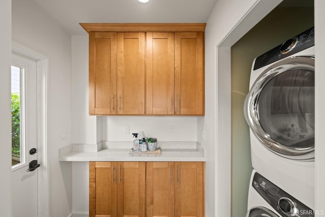 clothes washing area featuring stacked washer / drying machine and cabinet space