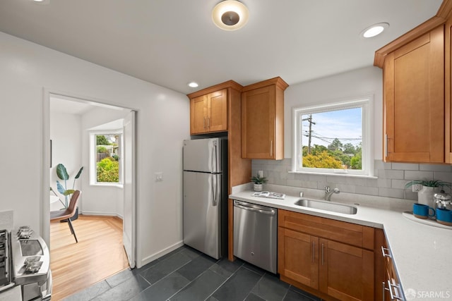 kitchen with brown cabinetry, stainless steel appliances, light countertops, backsplash, and a sink