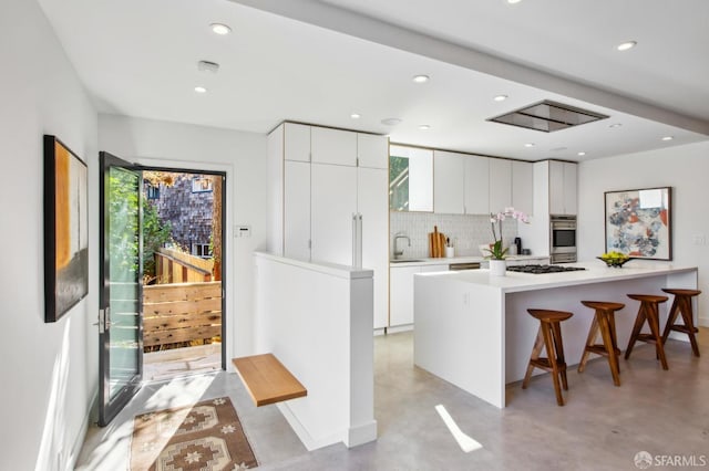 kitchen with white cabinetry, backsplash, a kitchen breakfast bar, gas cooktop, and stainless steel double oven