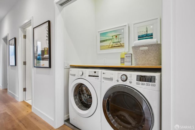 clothes washing area with washing machine and clothes dryer and light hardwood / wood-style flooring