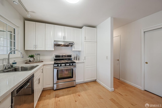 kitchen featuring dishwashing machine, under cabinet range hood, a sink, stainless steel gas range oven, and light wood finished floors
