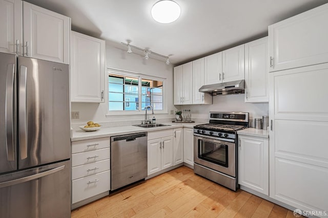 kitchen with light countertops, white cabinetry, under cabinet range hood, appliances with stainless steel finishes, and a sink