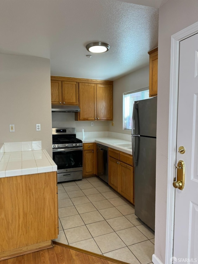 kitchen featuring a textured ceiling, stainless steel appliances, kitchen peninsula, tile countertops, and light tile patterned flooring