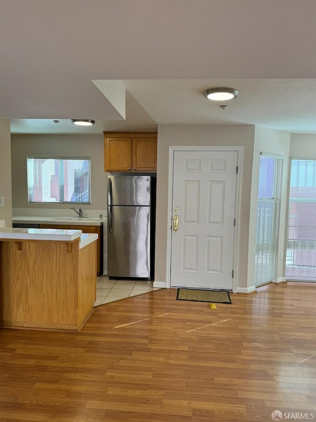 kitchen with kitchen peninsula, a kitchen bar, sink, light hardwood / wood-style flooring, and stainless steel fridge