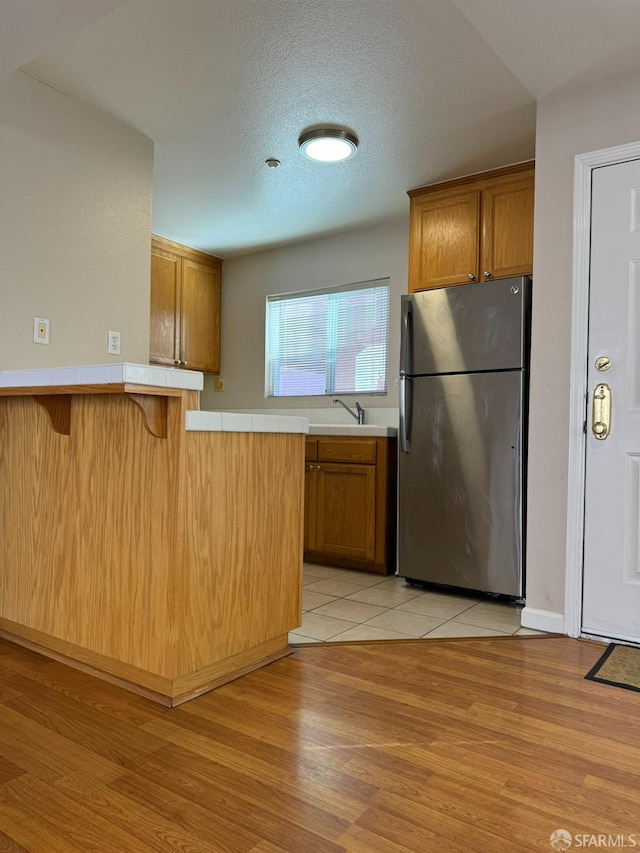 kitchen featuring a kitchen bar, kitchen peninsula, light hardwood / wood-style floors, stainless steel refrigerator, and sink