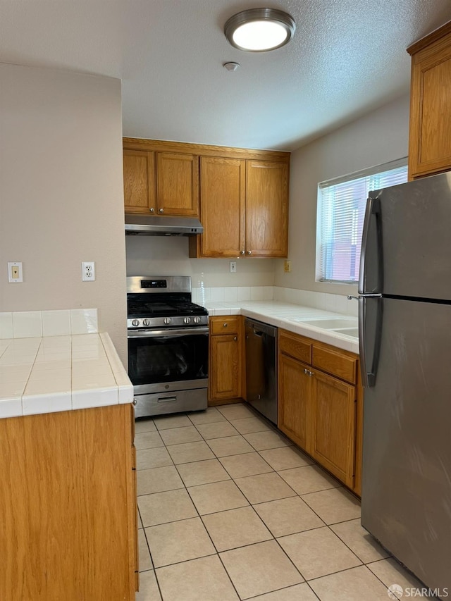 kitchen featuring sink, appliances with stainless steel finishes, tile counters, and light tile patterned flooring