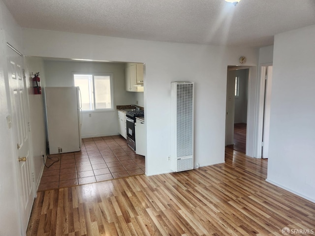 kitchen with white cabinetry, a textured ceiling, gas range, light hardwood / wood-style flooring, and white refrigerator