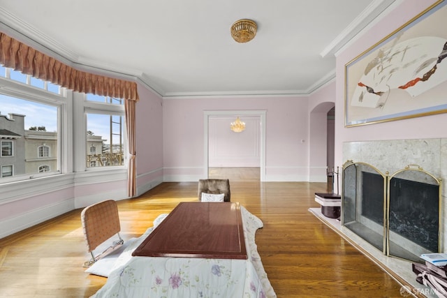 dining room with crown molding, light wood-style flooring, a fireplace, and arched walkways