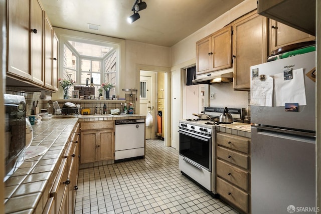 kitchen featuring a sink, tile counters, white appliances, and under cabinet range hood