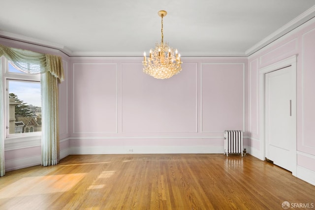 spare room featuring radiator, light wood-style flooring, crown molding, a decorative wall, and a chandelier