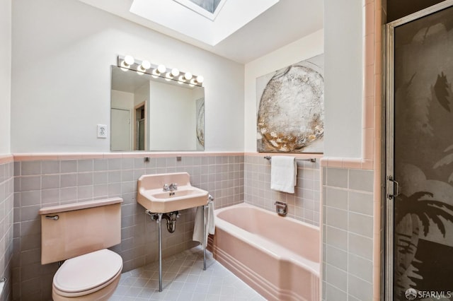 bathroom featuring toilet, a skylight, plus walk in shower, tile walls, and tile patterned floors