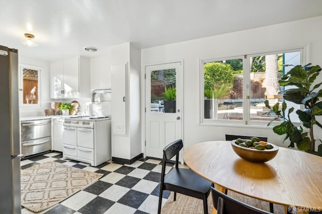 kitchen featuring white stove, stainless steel refrigerator, and white cabinetry