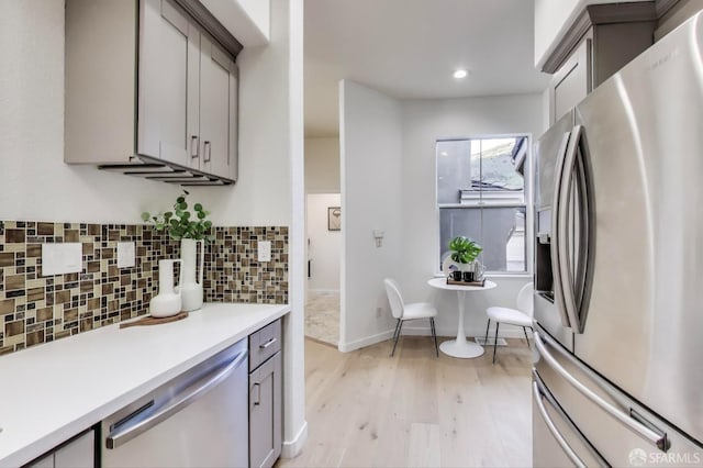 kitchen with light wood-type flooring, gray cabinets, tasteful backsplash, and appliances with stainless steel finishes