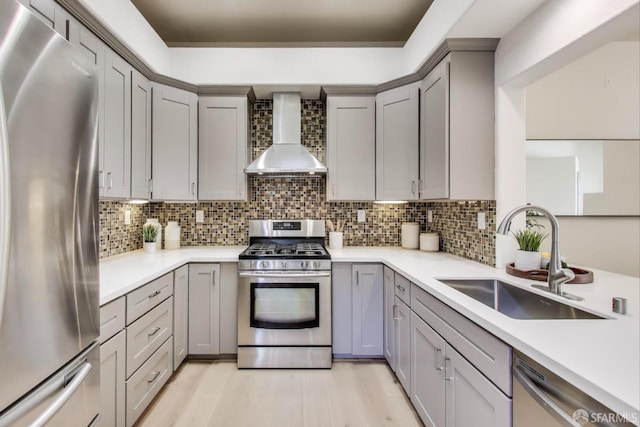 kitchen featuring sink, light hardwood / wood-style flooring, stainless steel appliances, decorative backsplash, and wall chimney range hood