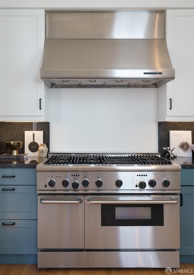 49 Hill St, San Francisco, CA 94110 - kitchen with range with two ovens, wall chimney exhaust hood, white cabinetry, decorative backsplash, and dark stone countertops