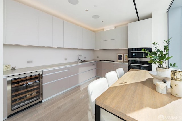 kitchen with sink, beverage cooler, light hardwood / wood-style flooring, white cabinets, and black appliances