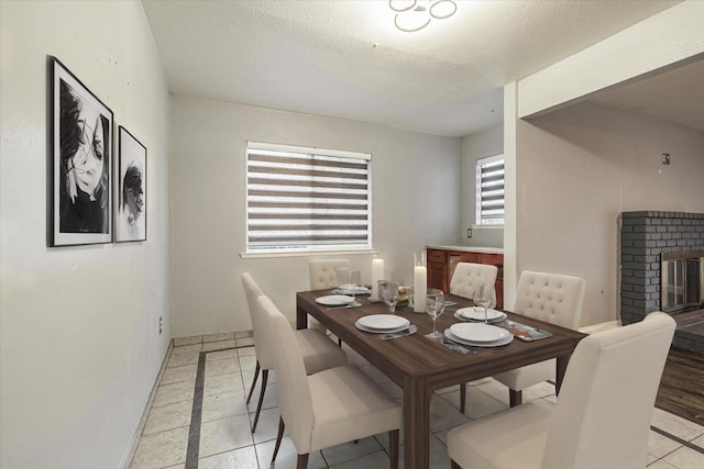 dining room featuring light tile patterned floors, a textured ceiling, and a brick fireplace