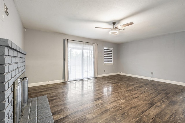 unfurnished living room featuring ceiling fan, dark wood-type flooring, and a brick fireplace