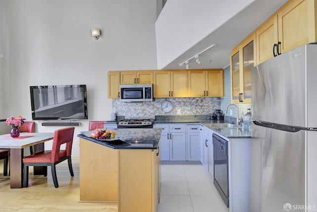 kitchen featuring a kitchen island, glass insert cabinets, appliances with stainless steel finishes, light brown cabinets, and a sink