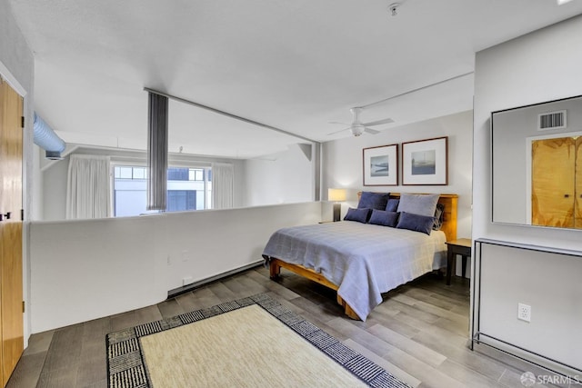 bedroom with ceiling fan, visible vents, baseboard heating, and wood finished floors