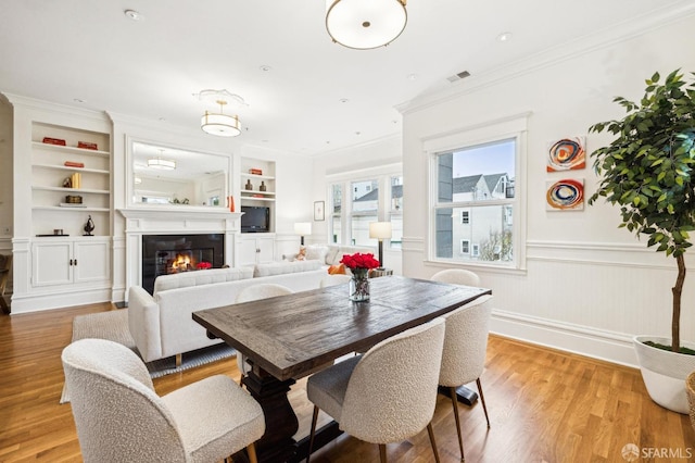 dining room with ornamental molding, light hardwood / wood-style floors, and built in features