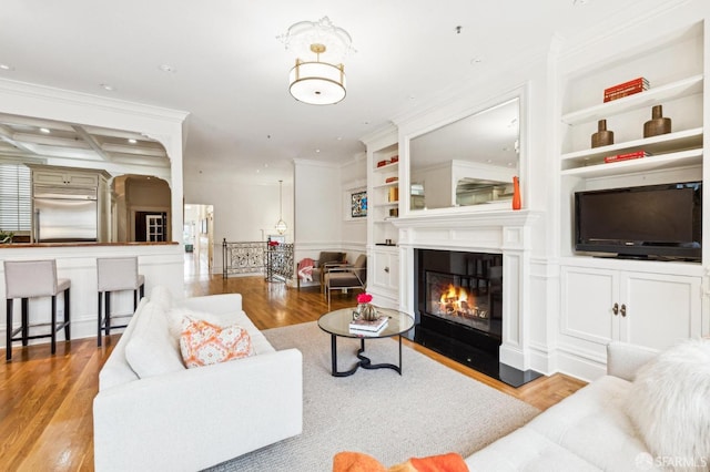 living room with built in shelves, coffered ceiling, crown molding, beam ceiling, and light hardwood / wood-style floors