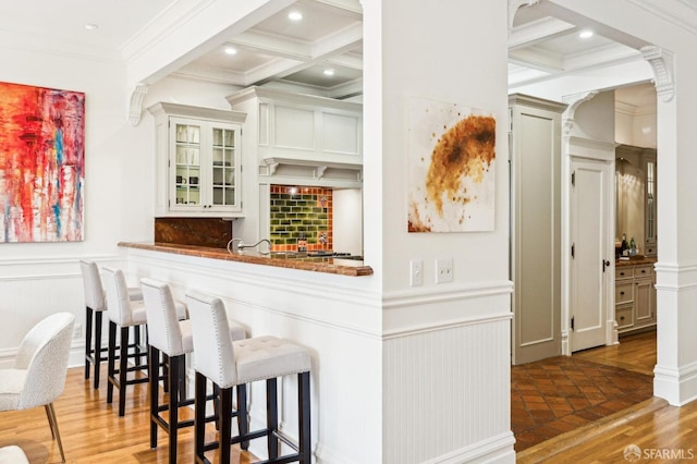 bar featuring ornate columns, coffered ceiling, dark wood-type flooring, and beam ceiling