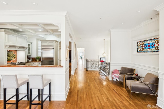 kitchen with coffered ceiling, a kitchen breakfast bar, kitchen peninsula, stainless steel appliances, and light hardwood / wood-style floors