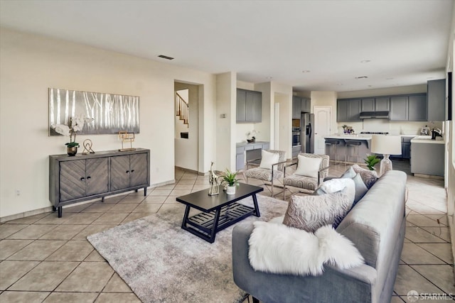 living area featuring light tile patterned floors, stairway, visible vents, and baseboards