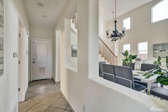 hallway with light tile patterned floors, stairway, a towering ceiling, and an inviting chandelier