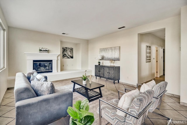 tiled living area with a glass covered fireplace, visible vents, and baseboards