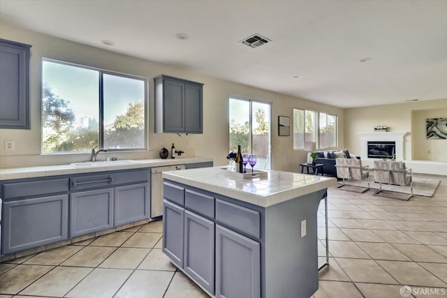 kitchen featuring tile countertops, light tile patterned flooring, a sink, visible vents, and a glass covered fireplace