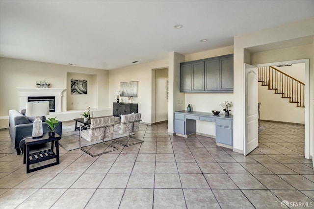 living area with light tile patterned floors, baseboards, a glass covered fireplace, built in study area, and stairs