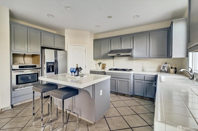 kitchen with tile counters, oven, fridge with ice dispenser, under cabinet range hood, and a sink