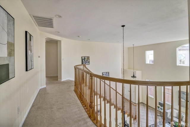 hallway with light colored carpet, baseboards, visible vents, and an upstairs landing