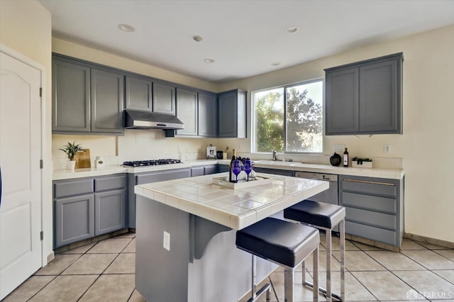 kitchen featuring tile countertops, light tile patterned floors, gas cooktop, under cabinet range hood, and a center island