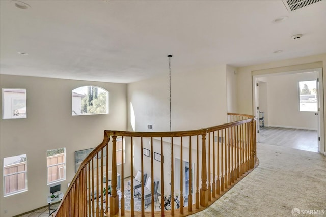 corridor with carpet floors, an upstairs landing, visible vents, and a healthy amount of sunlight