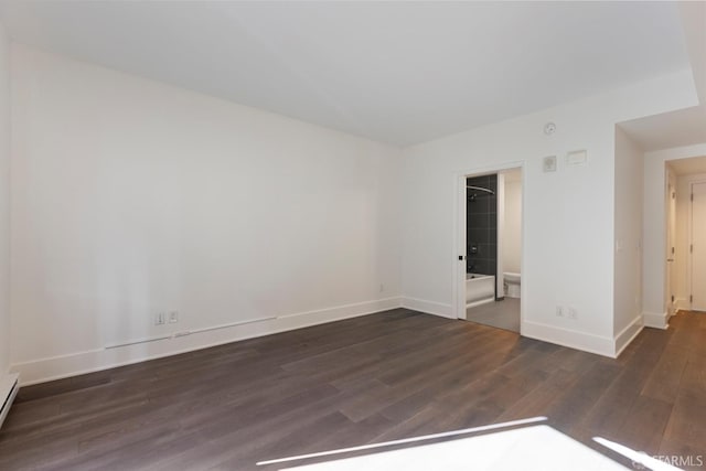 spare room featuring a baseboard heating unit, baseboards, and wood finished floors