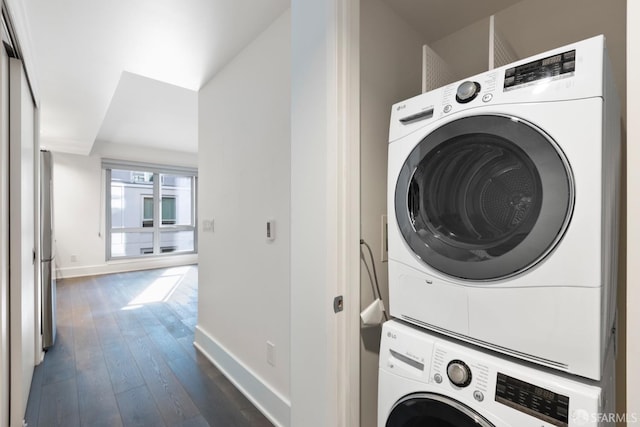 laundry area with stacked washer and dryer, laundry area, baseboards, and dark wood finished floors