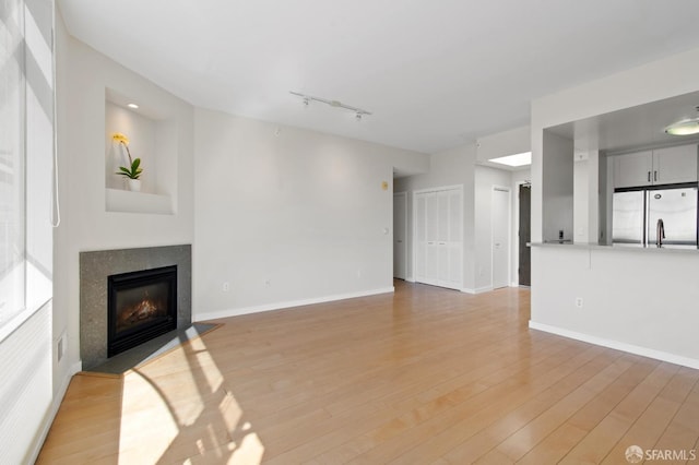 1600 Webster St Unit 409, San Francisco, CA 94115 - unfurnished living room featuring track lighting, light wood-style flooring, baseboards, and a glass covered fireplace